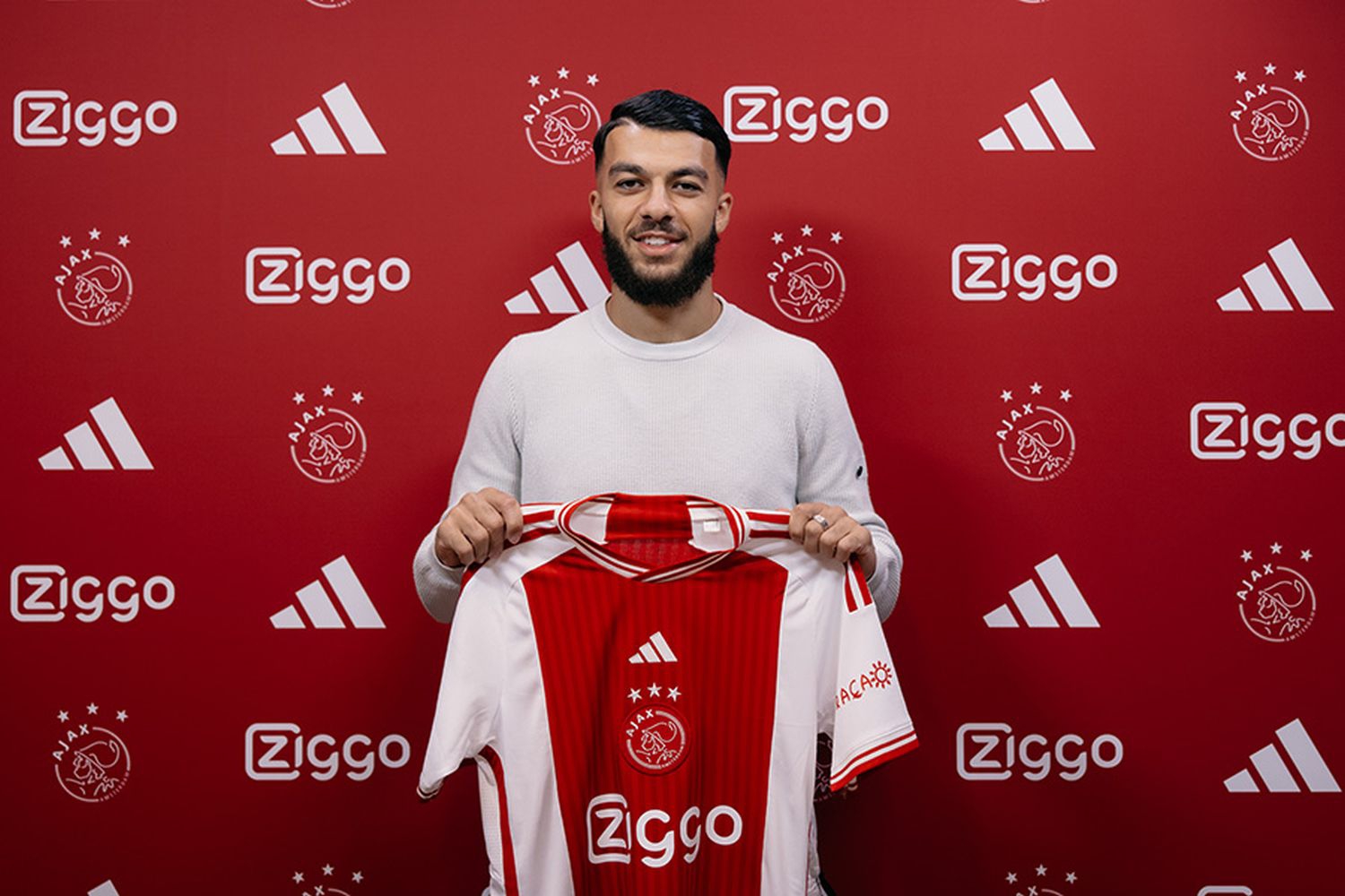  Georges Mikautadze, a Georgian striker, holds a jersey with his name on it while posing in front of a red background with white logos.